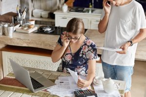 Couple managing home expenses together at the kitchen table with documents, laptop, and calculator.